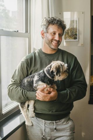 Happy adult man holding purebred dog while standing near window