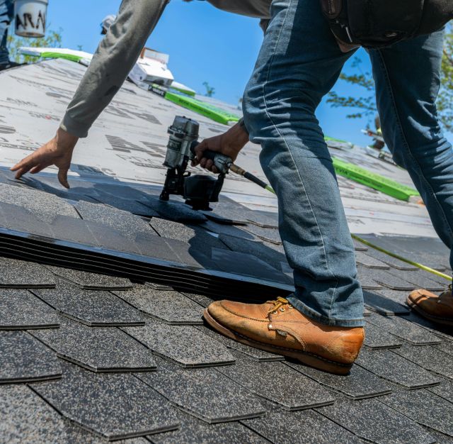 Roofer using nail gun for shingle installation on residential roof.